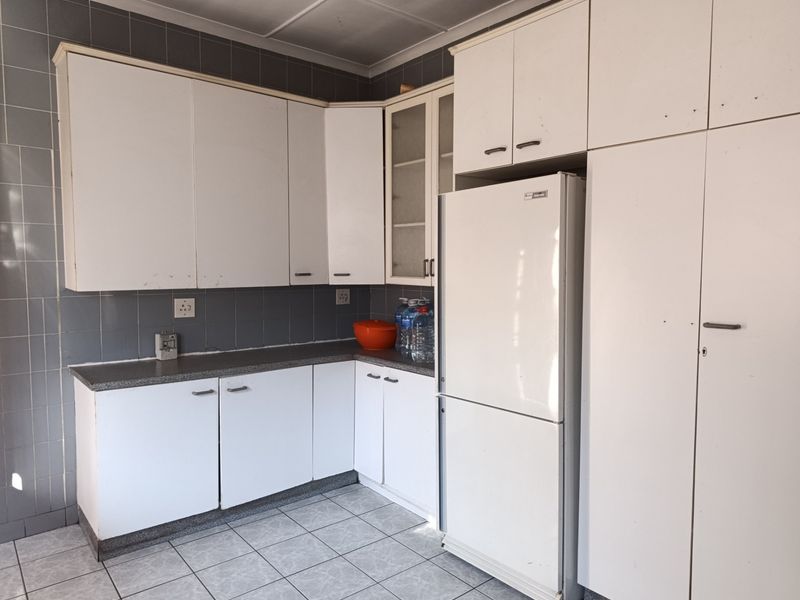 A functional kitchen featuring white built-in cabinetry, grey tiled backsplash, and tiled flooring, offering a clean but dated aesthetic ready for modernization.
