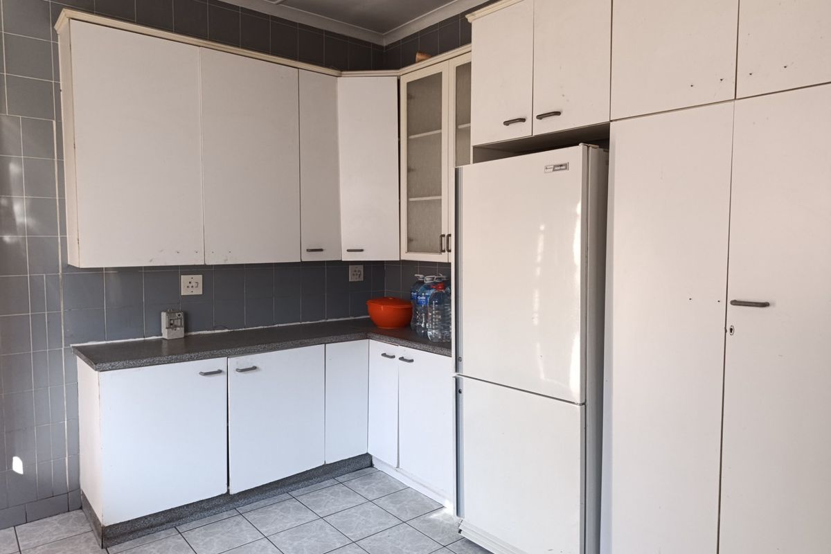 A functional kitchen featuring white built-in cabinetry, grey tiled backsplash, and tiled flooring, offering a clean but dated aesthetic ready for modernization.