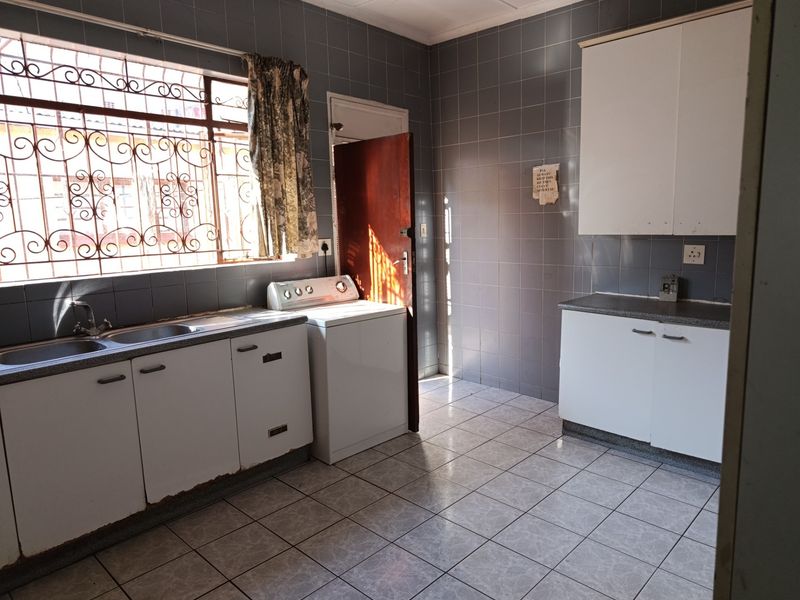 Functional laundry room featuring tiled walls and floors, built-in cabinetry, and a double basin sink with security bars on the window.