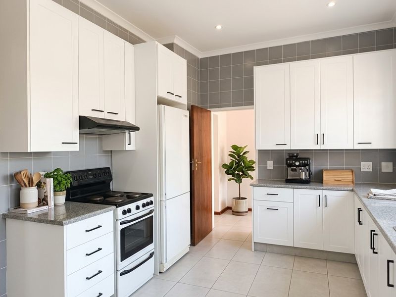 A well-maintained kitchen featuring white cabinetry, granite countertops, grey tiled backsplash, and a freestanding stove with an extractor fan.