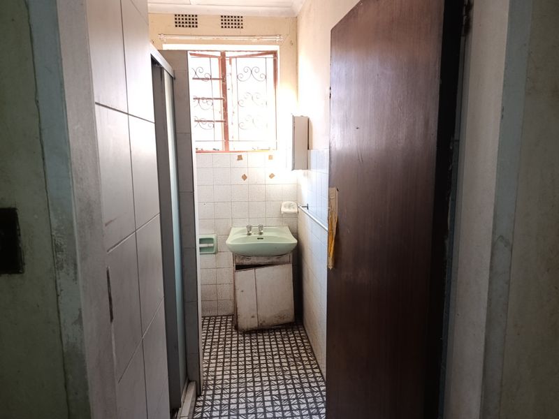 A dated bathroom featuring a pedestal basin, tiled flooring, and a shower enclosure, requiring modernization and cosmetic updates to improve its condition.