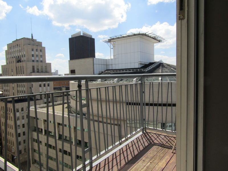 A balcony with timber decking and a metal balustrade, offering an elevated urban view of surrounding city buildings.