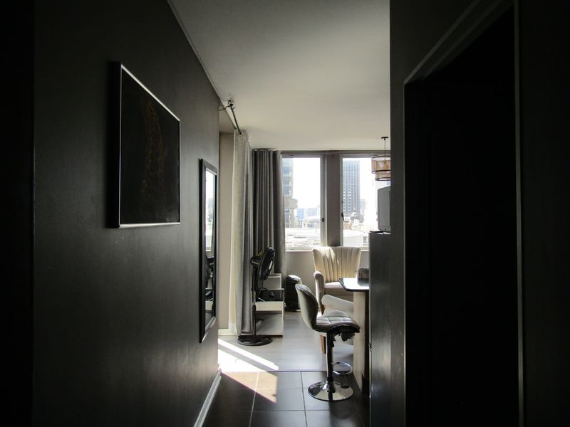 An open-plan living area featuring dark wall finishes, large windows with natural light, and tiled flooring, offering a view of the surrounding city.