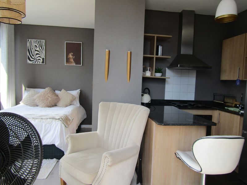 An open-plan studio apartment featuring a compact kitchen with stone countertops and integrated appliances, seamlessly flowing into the bedroom area.