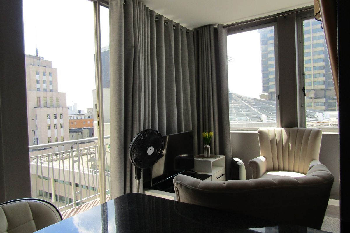 A bright living area featuring large windows and a sliding glass door that opens onto a balcony with urban city views.