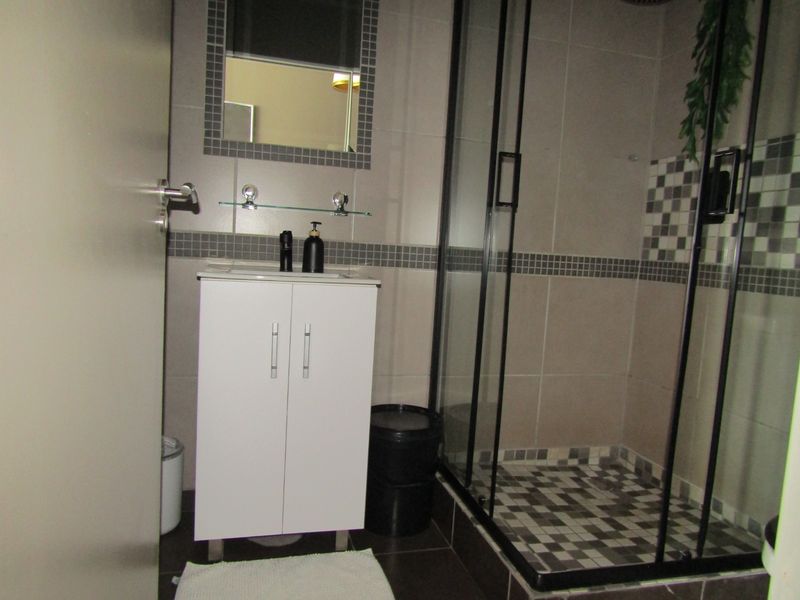 Modern bathroom featuring a white vanity cabinet, a glass-enclosed shower with decorative mosaic tile accents, and neutral wall tiling.