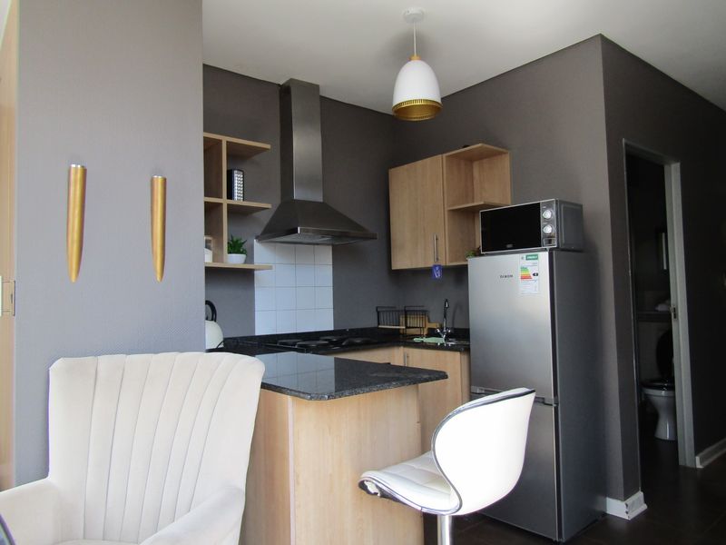Compact kitchen featuring modern dark grey walls, light wood cabinetry, granite countertops, and a stainless steel extractor fan.
