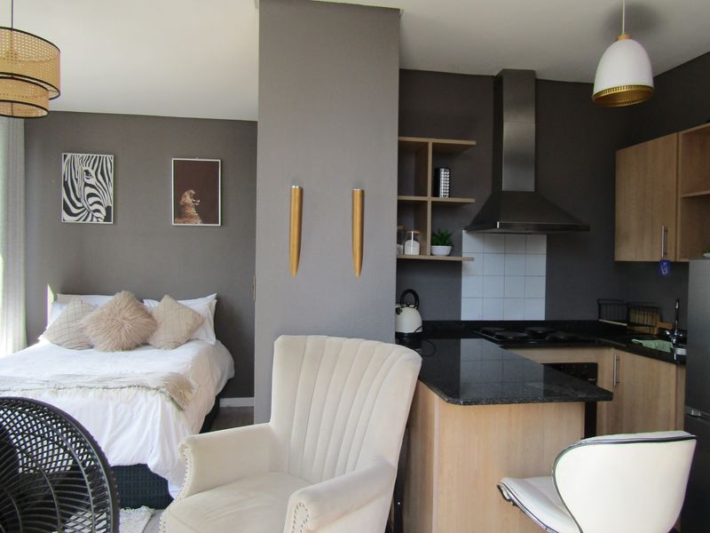 An open-plan studio apartment featuring a compact kitchen with granite countertops and integrated cabinetry, seamlessly flowing into the bedroom area.