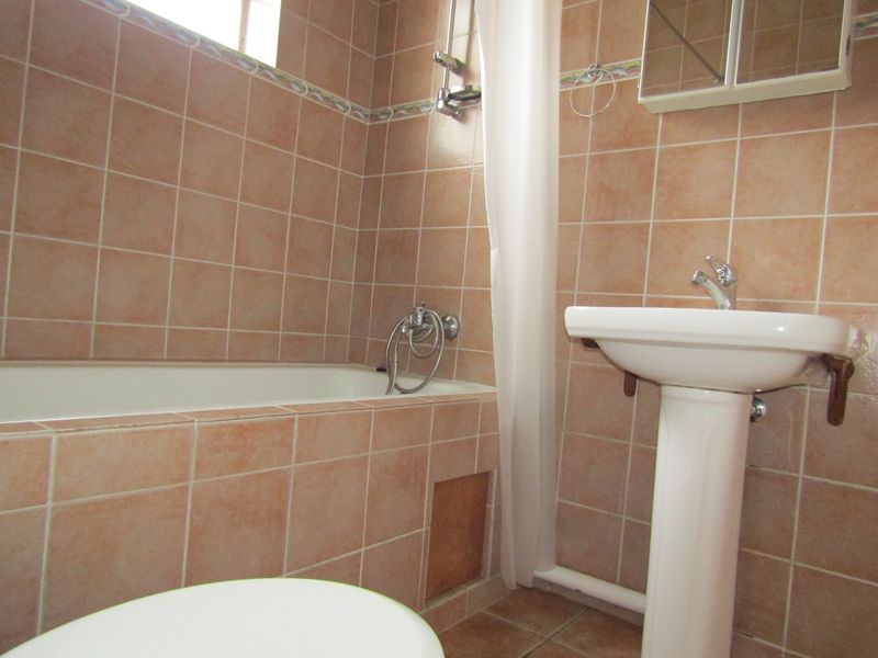 A dated bathroom featuring a tiled bathtub, pedestal sink, and wall-mounted medicine cabinet, requiring cosmetic updates to modernize the space.