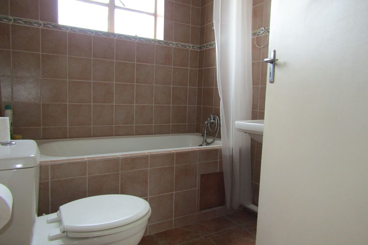 A dated bathroom featuring ceramic wall and floor tiles, a built-in bathtub, and a wall-mounted basin.