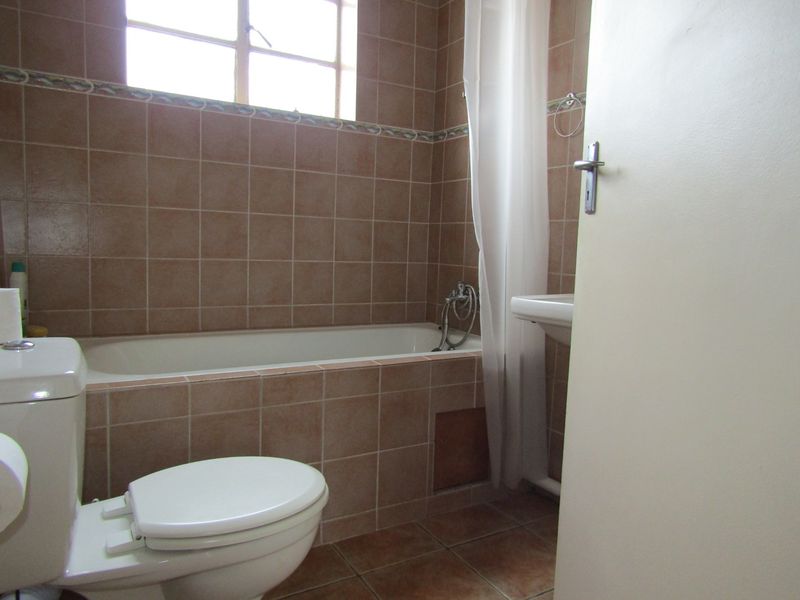 A dated bathroom featuring ceramic wall and floor tiles, a built-in bathtub, and a wall-mounted basin.