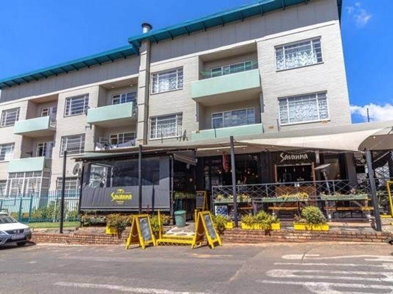 Exterior view of a multi-story apartment building featuring balconies and a ground-floor commercial space with an outdoor seating area.