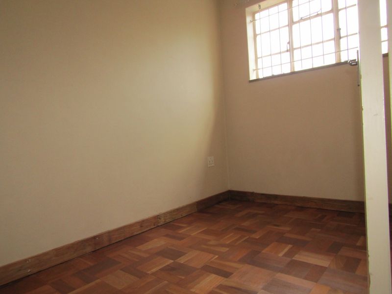 An empty bedroom featuring classic parquet flooring, a window with security burglar bars, and neutral wall finishes.