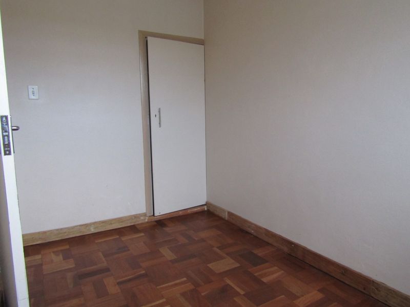 An empty bedroom featuring original parquet flooring and a built-in cupboard, presenting a blank canvas for renovation or interior design updates.