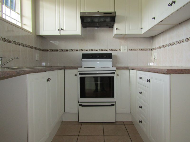 A functional kitchen featuring white cabinetry, laminate countertops, a freestanding stove with extractor fan, and tiled flooring.