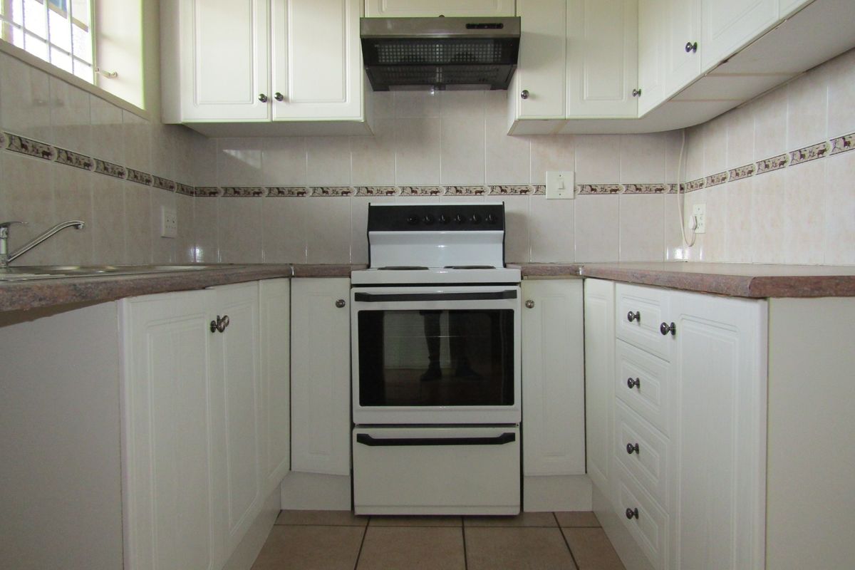 A functional kitchen featuring white cabinetry, laminate countertops, a freestanding stove with extractor fan, and tiled flooring.