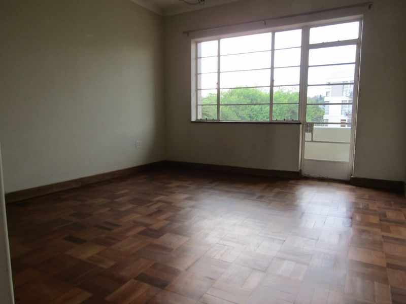 An empty bedroom featuring classic parquet flooring, large steel-framed windows, and direct access to a balcony.