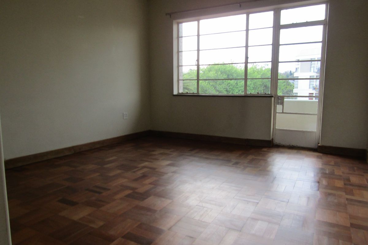 An empty bedroom featuring classic parquet flooring, large steel-framed windows, and direct access to a balcony.