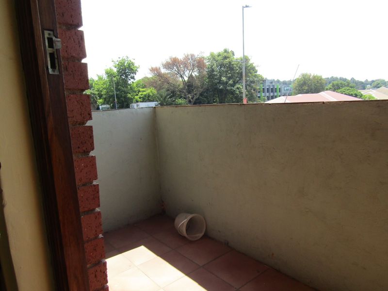 A compact balcony featuring tiled flooring and a solid masonry balustrade, offering an outdoor space with views of the surrounding neighborhood.