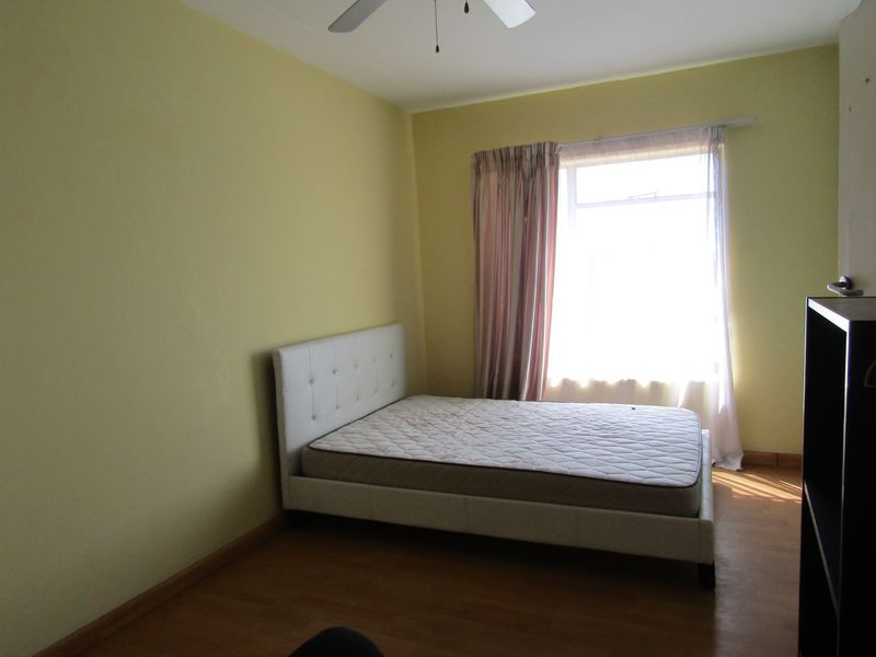 A standard bedroom featuring laminate flooring, a ceiling fan, and a window with curtains, offering a functional space ready for personalization.