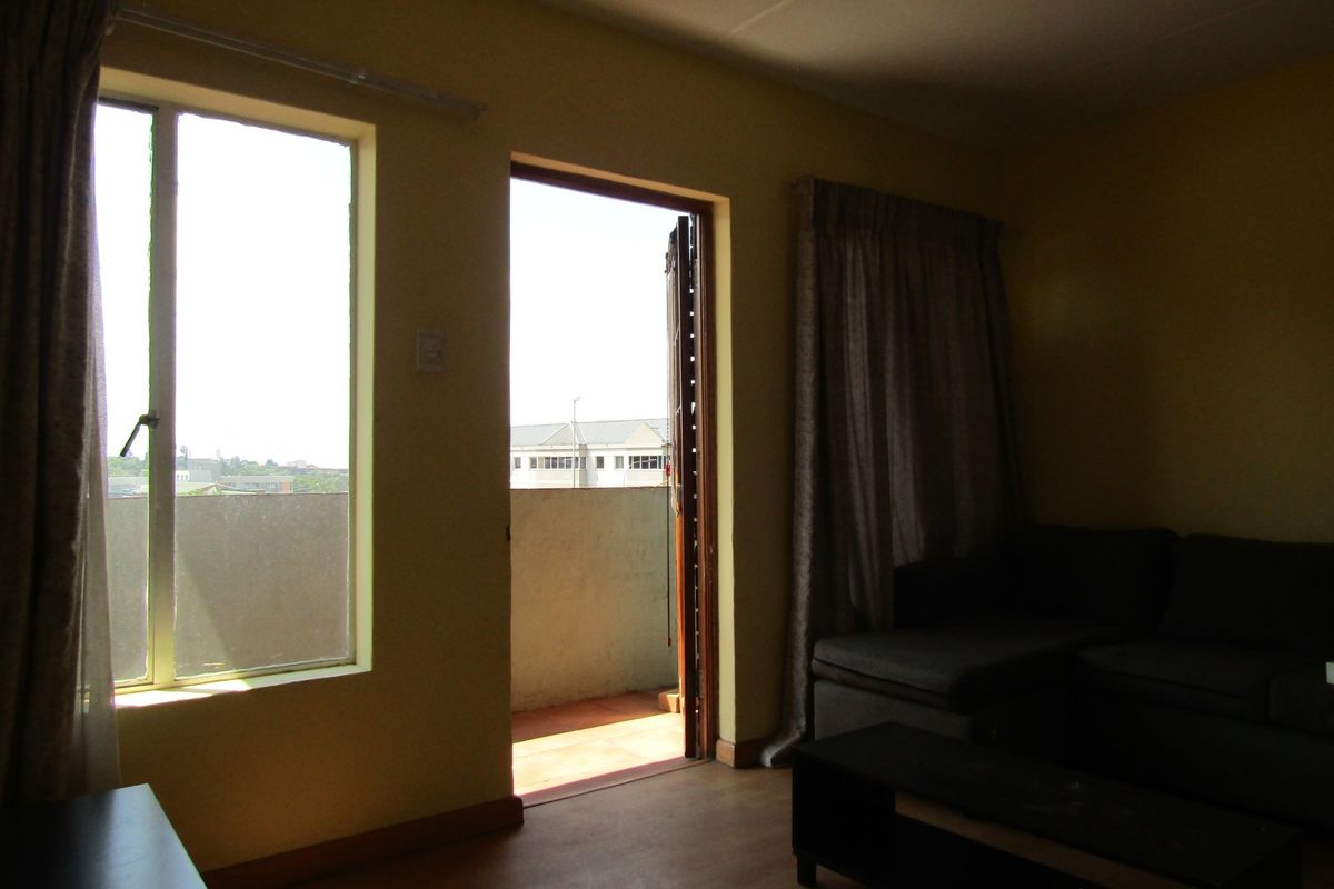 A living room area featuring laminate flooring and direct access to an outdoor balcony through a sliding door.