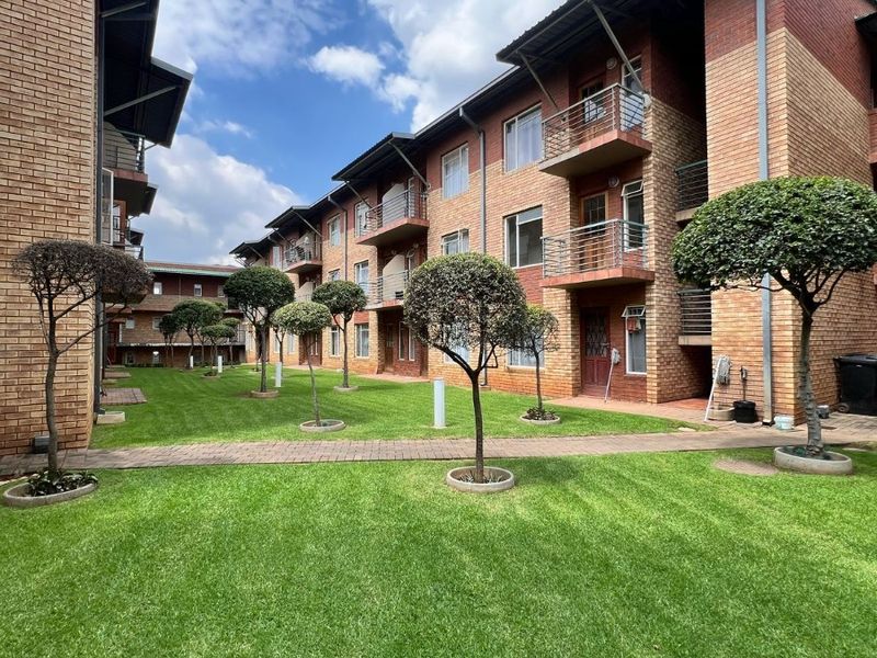 A view of the apartment complex rear facade featuring face brick construction, private balconies with metal railings, and a well-maintained communal garden area.