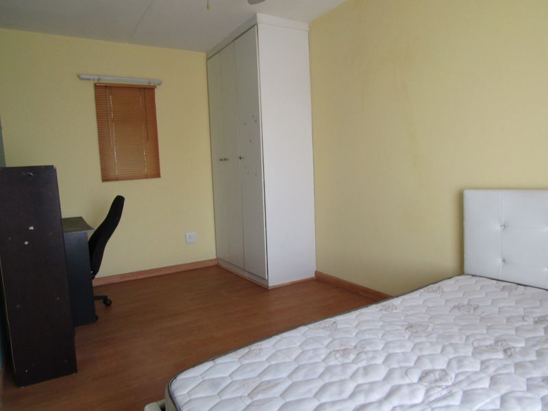 A functional bedroom featuring laminate flooring, a built-in wardrobe, and a window with a fitted venetian blind.