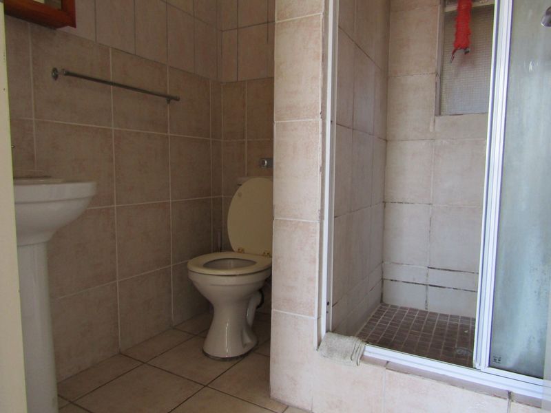A functional bathroom featuring a pedestal basin, toilet, and a separate shower enclosure with tiled finishes throughout.