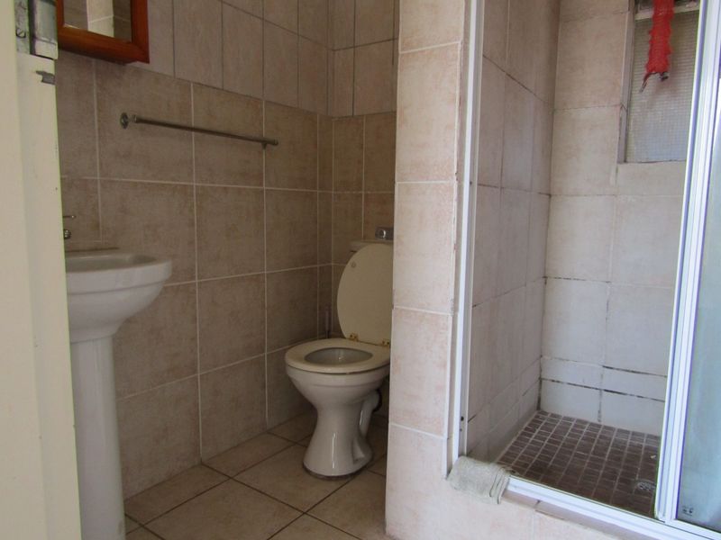 A functional bathroom featuring a pedestal basin, toilet, and a tiled shower enclosure with neutral wall and floor tiling.