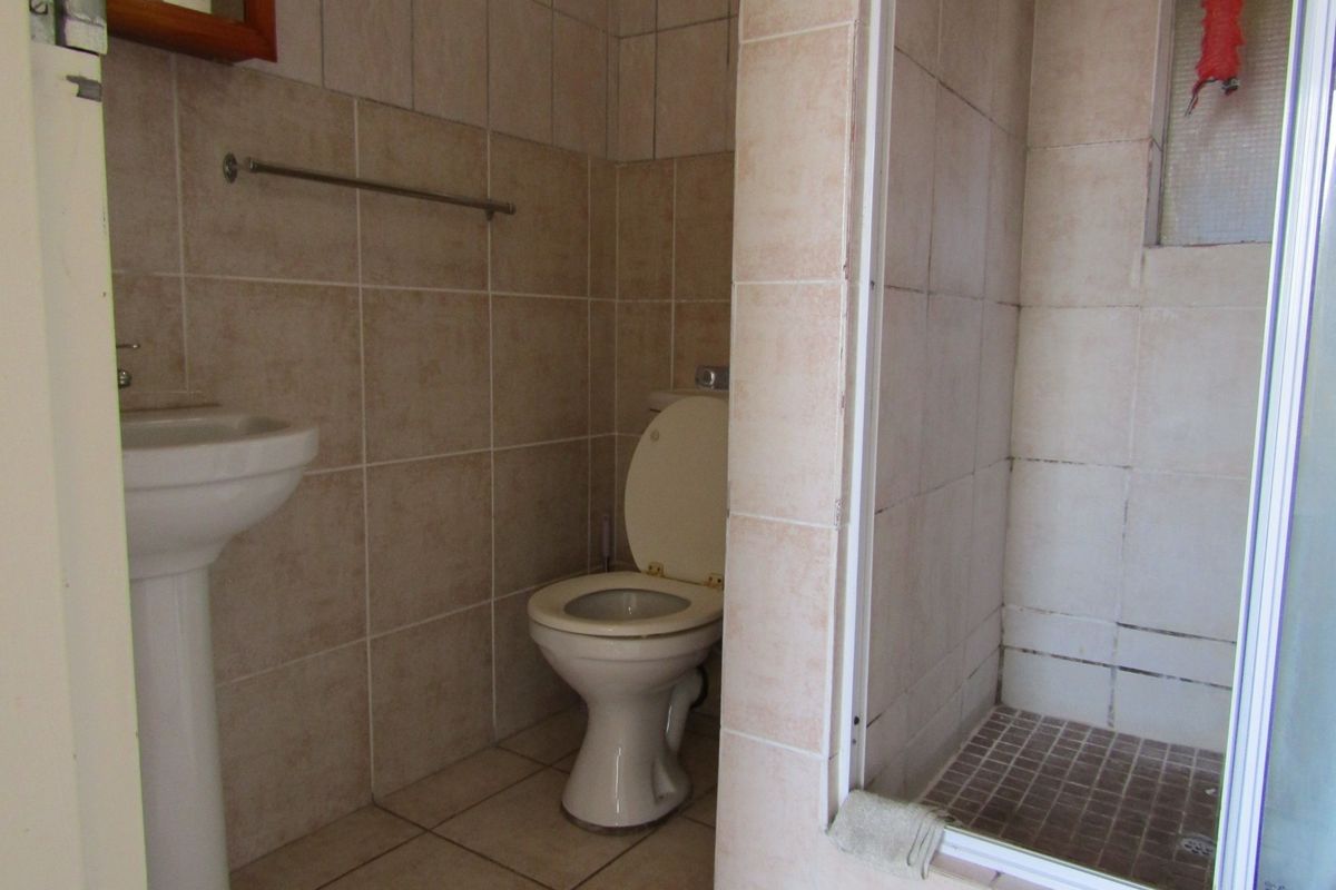 A functional bathroom featuring a pedestal basin, toilet, and a tiled shower enclosure with neutral wall and floor tiling.
