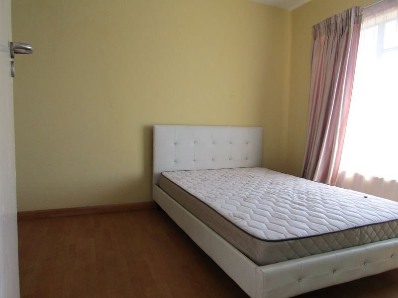 A simple bedroom featuring laminate flooring and natural light from a window with curtain tracks.