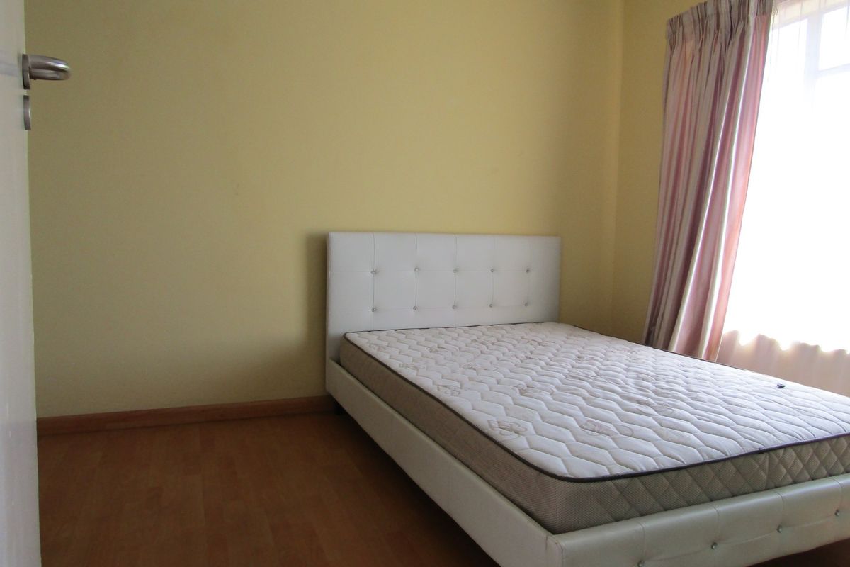 A simple bedroom featuring laminate flooring and natural light from a window with curtain tracks.