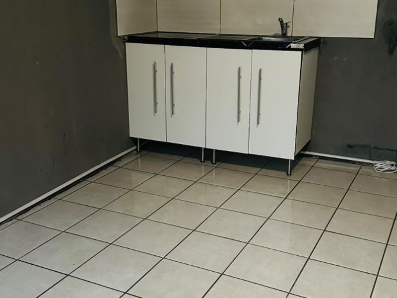 A compact kitchen area featuring white built-in cabinetry, a sink, and tiled flooring, currently requiring wall finishing and final touches.