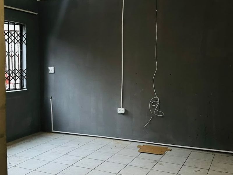An empty living room featuring tiled flooring, security bars on the window, and exposed electrical wiring, requiring cosmetic updates and finishing.