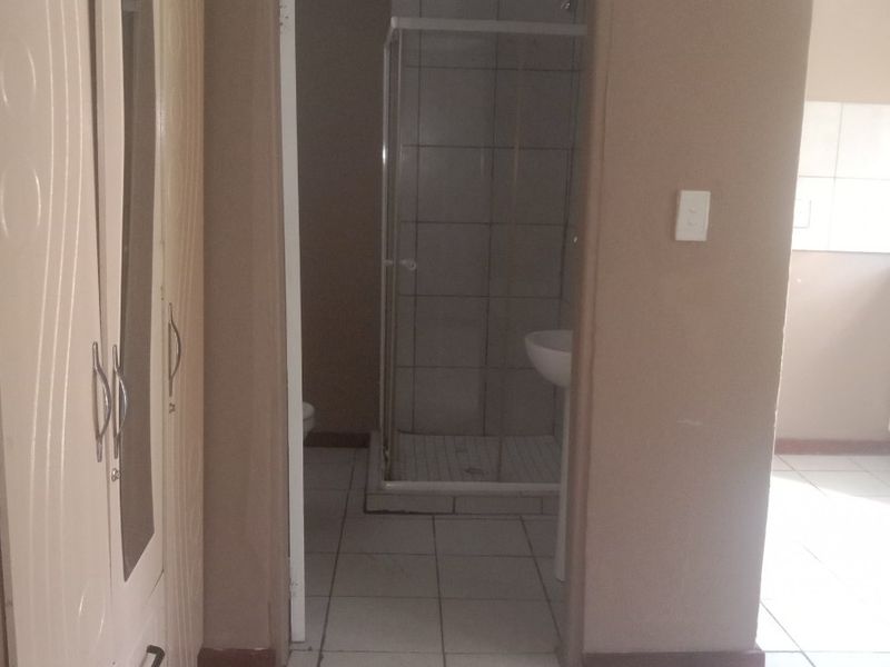 A functional bathroom featuring a shower enclosure and pedestal basin with neutral tiled finishes, accessible from the adjacent living area.