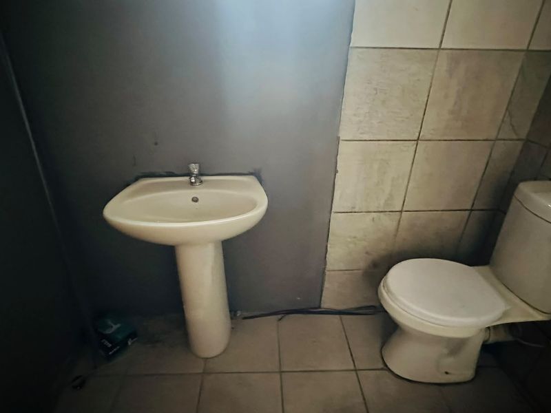 A compact bathroom featuring a pedestal basin and toilet with tiled flooring and partial wall tiling, requiring cosmetic updates to improve its condition.