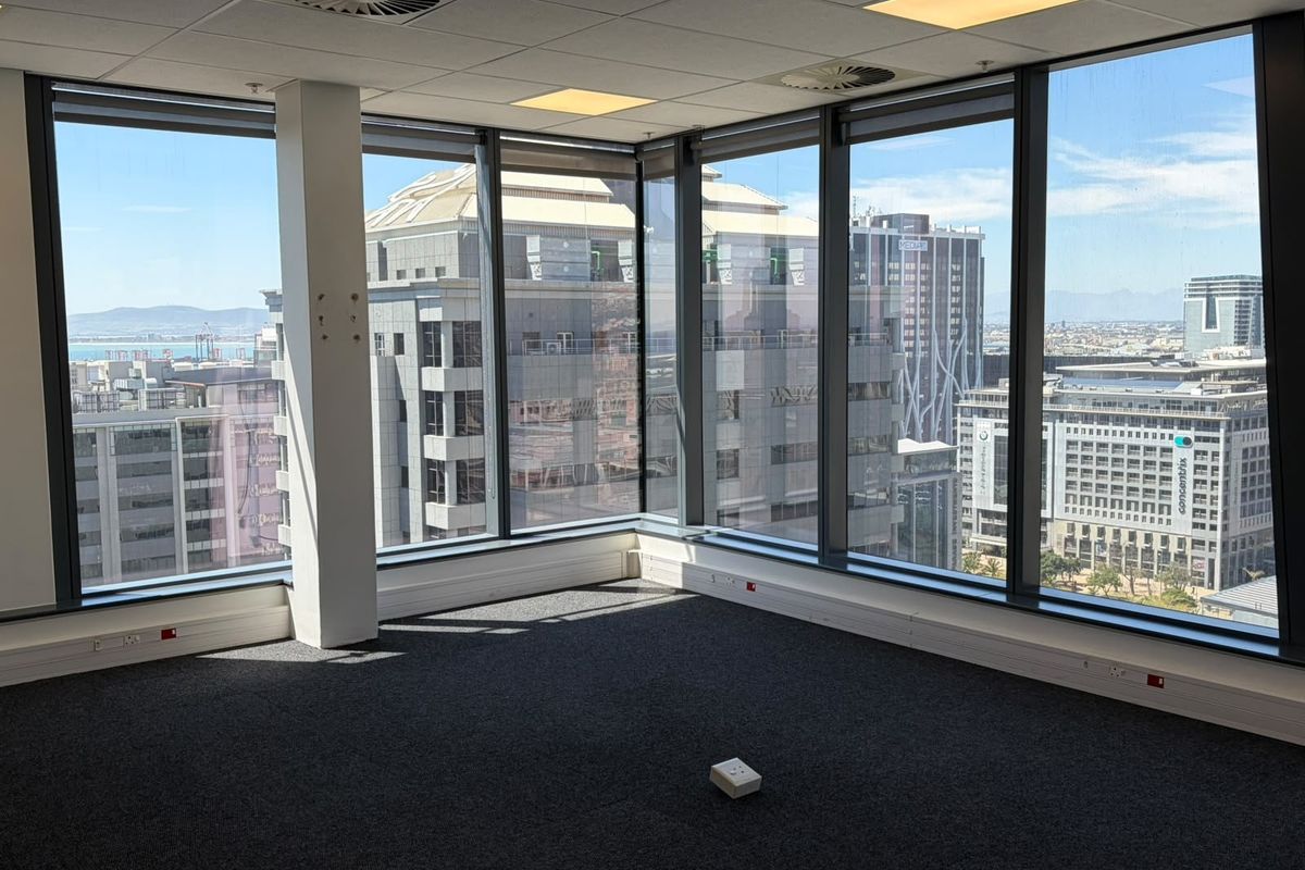 A bright, empty corner office space featuring floor-to-ceiling windows with expansive city views, carpeted flooring, and a modern suspended ceiling.