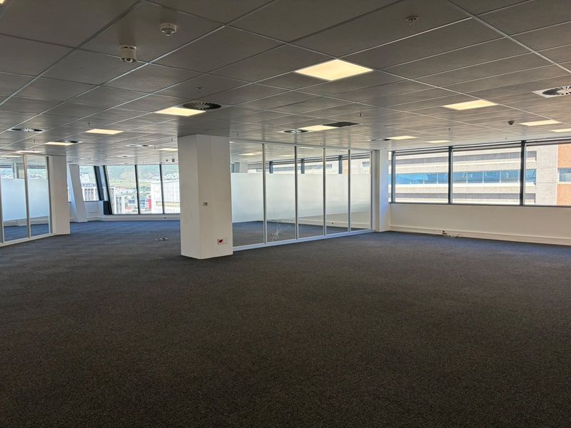 Spacious open-plan office area featuring suspended ceilings, recessed lighting, large windows with city views, and glass partitioning.