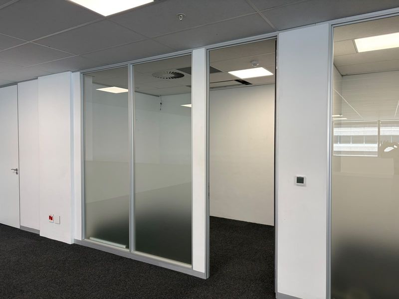 A modern, empty office space featuring glass partition walls, recessed ceiling lighting, and dark carpeting, providing a clean and professional environment.