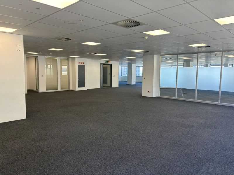 Spacious open-plan office area featuring carpeted flooring, suspended ceilings with recessed lighting, and glass-partitioned meeting rooms.