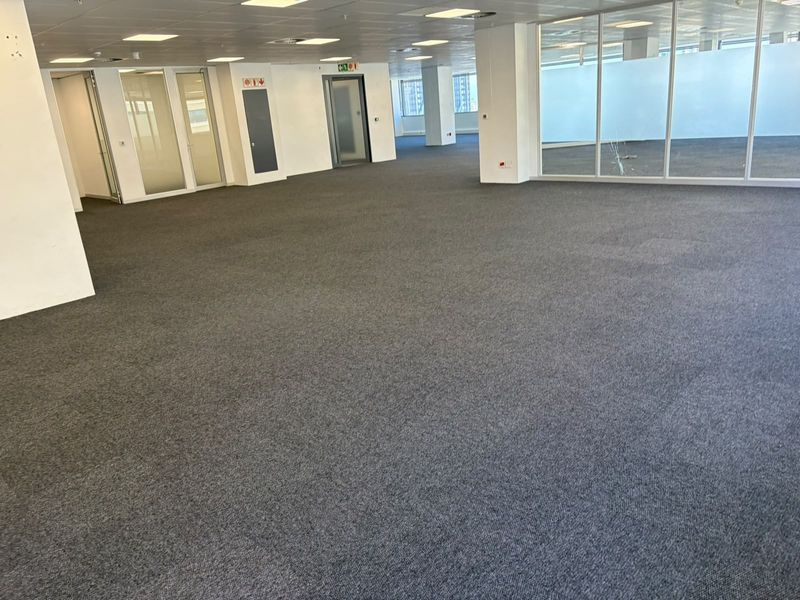 Spacious open-plan office area featuring carpeted flooring, suspended ceilings with recessed lighting, and glass partitioning, offering a versatile workspace environment.