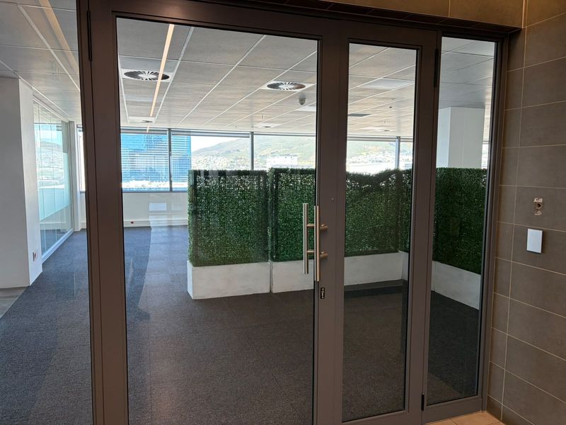 Modern office space featuring glass partition doors, suspended ceilings with recessed lighting, and large windows offering expansive views.