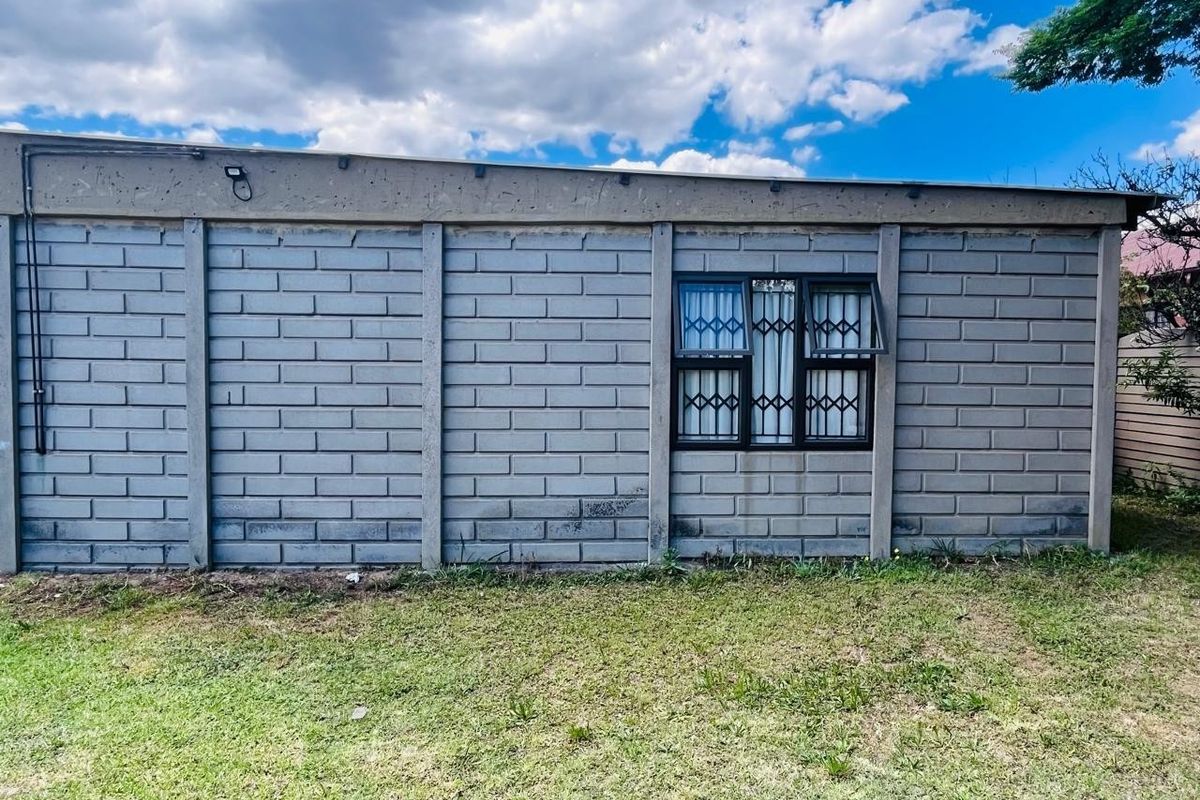 A view of the rear exterior wall constructed from precast concrete blocks, featuring a single window with security burglar bars.
