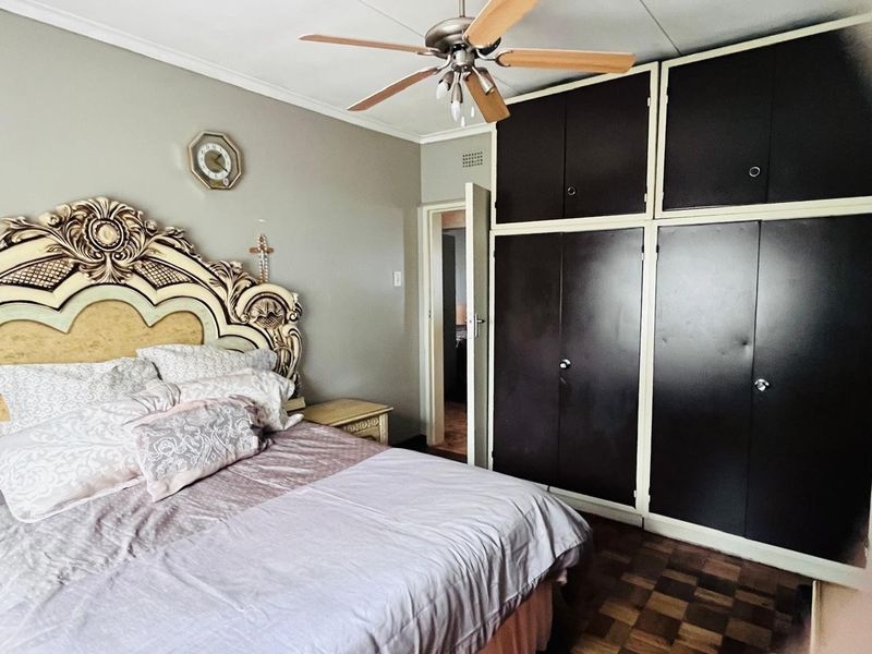 A bedroom featuring classic parquet flooring, a ceiling fan, and extensive built-in storage cupboards.