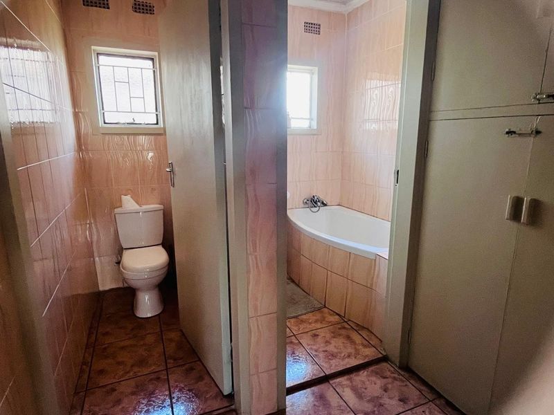 A dated bathroom featuring a separate toilet and bathtub area with original ceramic tiling and basic fixtures, offering potential for modern renovation.