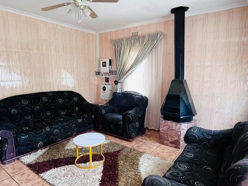 Living room featuring tiled walls, tiled flooring, a ceiling fan, and a prominent black freestanding fireplace.