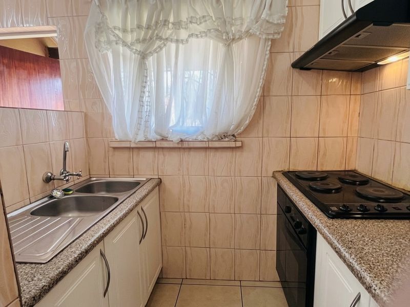 Compact kitchen featuring a double bowl sink, built-in oven, electric hob, extractor fan, and tiled finishes throughout.