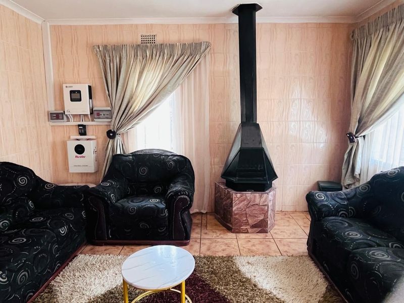 A living room featuring a prominent freestanding fireplace, tiled wall finishes, and a wall-mounted solar inverter system.
