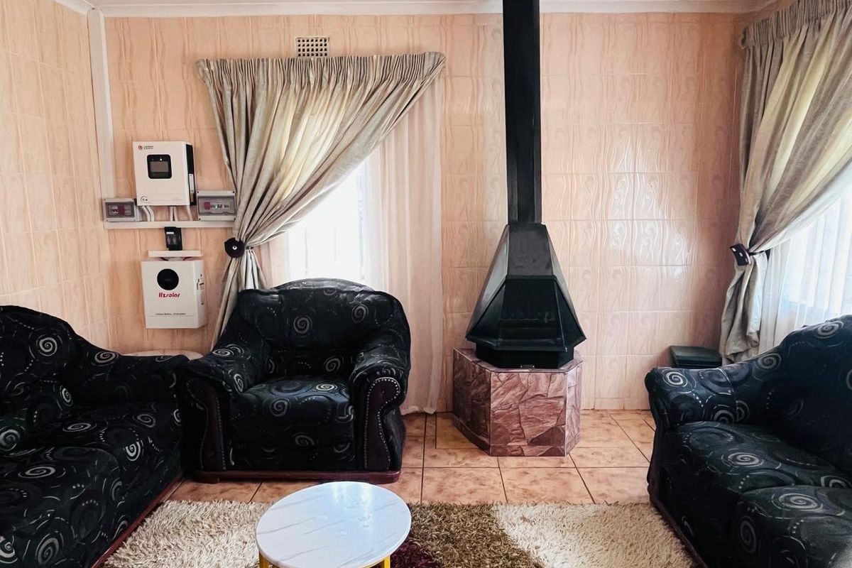 A living room featuring a prominent freestanding fireplace, tiled wall finishes, and a wall-mounted solar inverter system.
