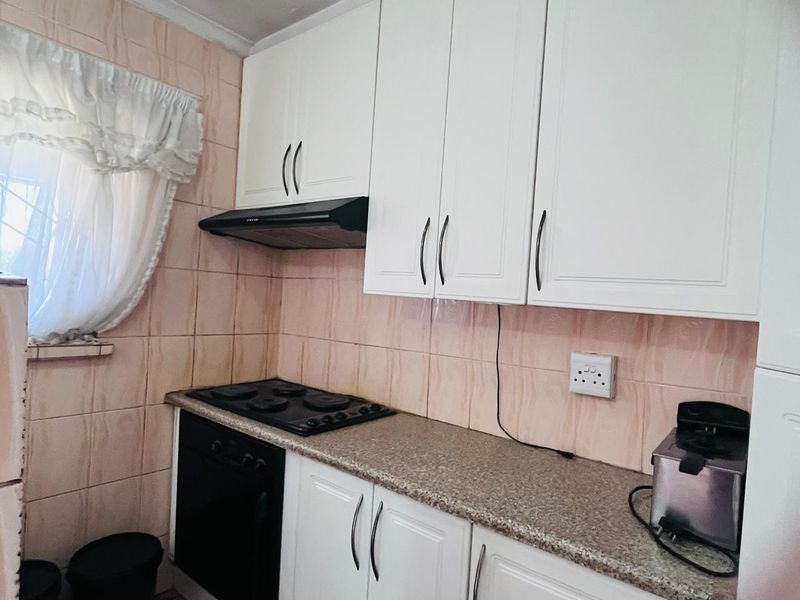 A functional kitchen featuring white cabinetry, granite countertops, a built-in oven, hob, and extractor fan with tiled splashbacks.